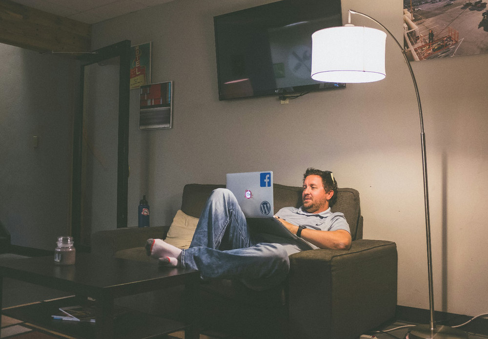 A person slumped on a sofa with their feet resting on a coffee table while holding an open laptop, highlighting the comfort and convenience that is an advantage of online counseling