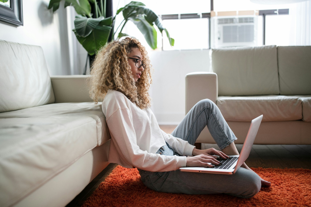 A person using a laptop while sitting on a rust carpet on the floor, showcasing comfort, an advantage of online counseling