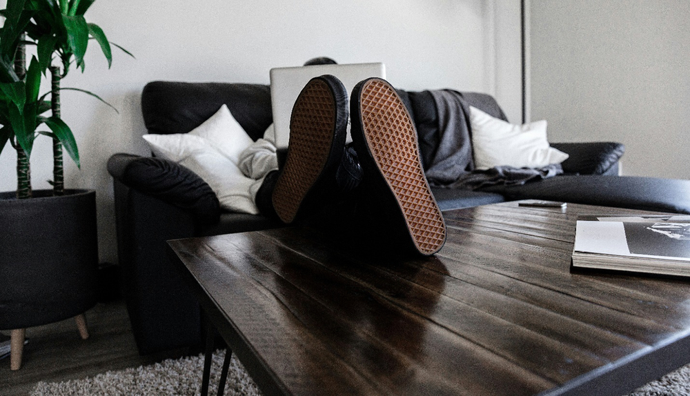 A person sits on a couch with their shoes resting on a coffee table while using a laptop, the convenience symbolizing the advantages of online counseling