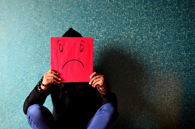 A man holding a mask with a sad face sits slumped on the floor