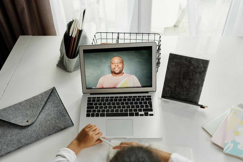 An elevated shot of a desk with a laptop on it with an image of a man on the screen and the hair, hands, and stationary visible of another person, showcasing what EMDR therapy from home may look like